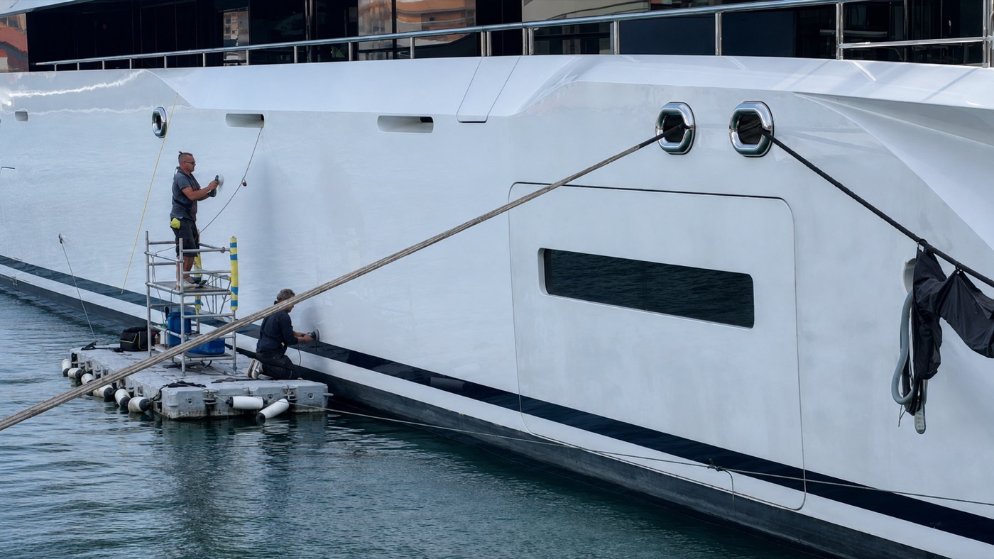An RMP Marine technician polishing the hull of the 87m Lurssen from a floating work platform.